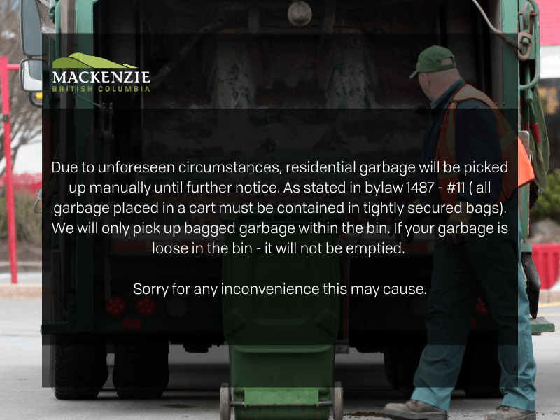 A worker stands behind a garbage truck about to pick up a garbage can.