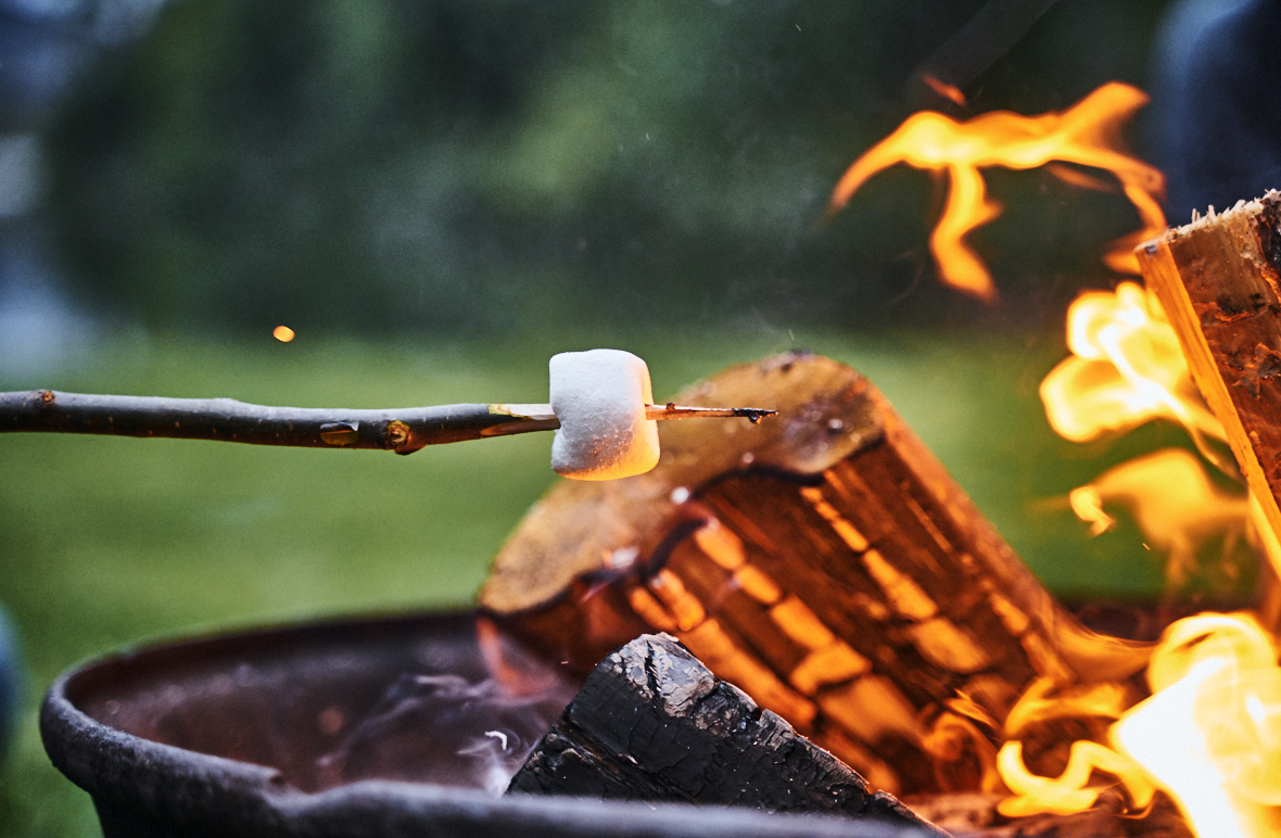 A marshmallow on a stick is roasted over a crackling camp fire