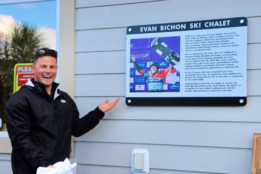 Evan Bichon stands excitedly beside a new sign that reads "Evan Bichon Ski Chalet"