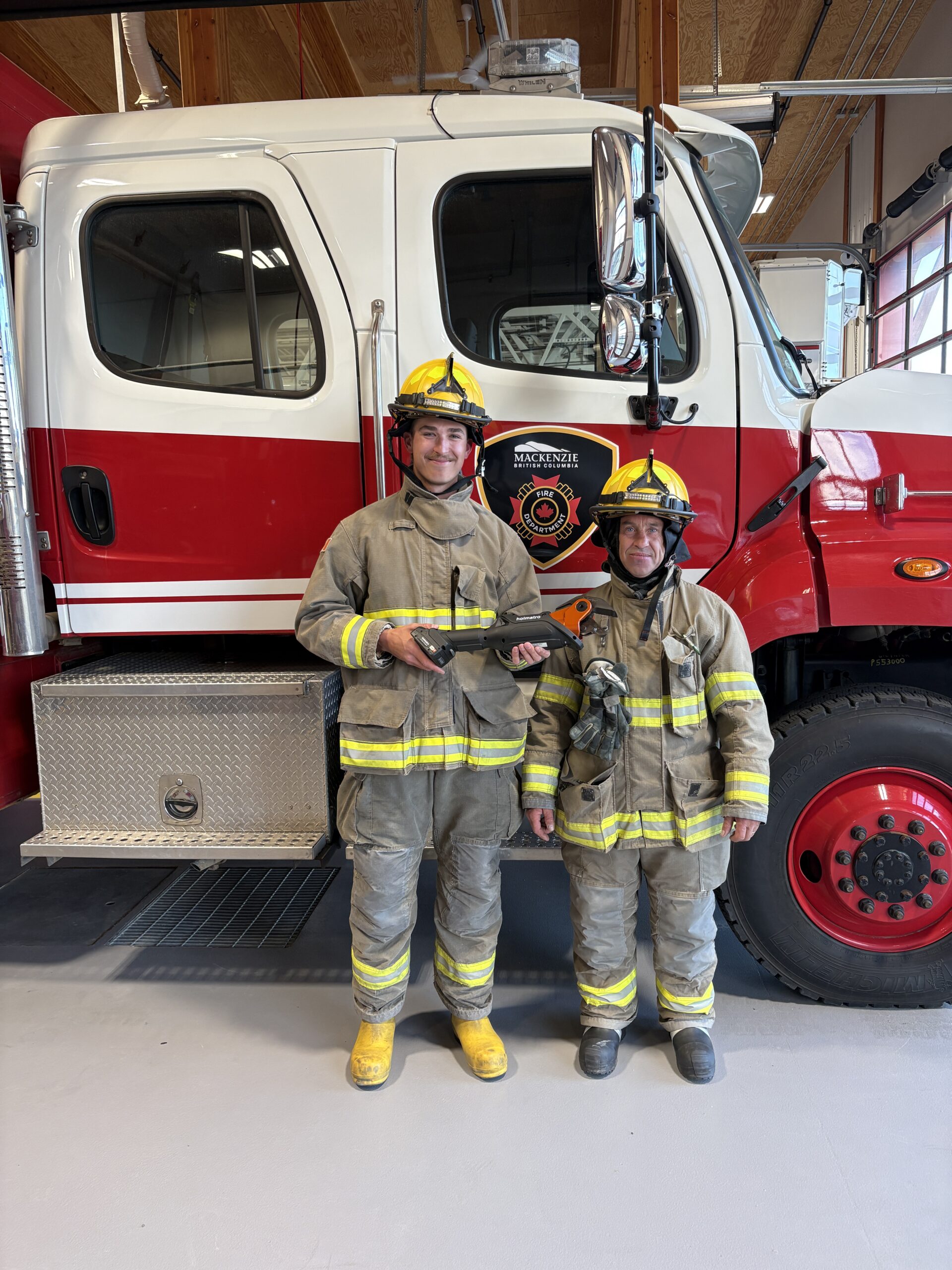 Two firefighters show off a new battery-operated mini cutter